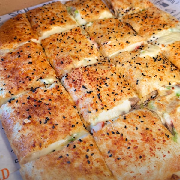 Close-up of a large, square, golden-brown flatbread cut into smaller squares, topped with sesame seeds.