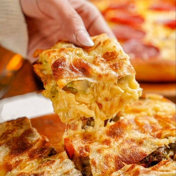 A hand lifts a cheesy, golden-brown square of baked pasta, stretching cheese from the dish.