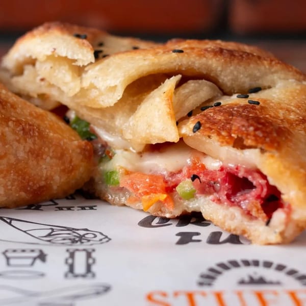 Close-up of a golden-brown stuffed pastry, cut open to reveal melted cheese, red meat, and vegetables.