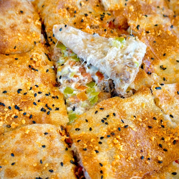 Close-up of a golden-brown savory pastry, cut to reveal melted cheese, ground meat, and diced vegetables.